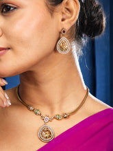 Close-up of a woman wearing a gold necklace and earrings with a blue background