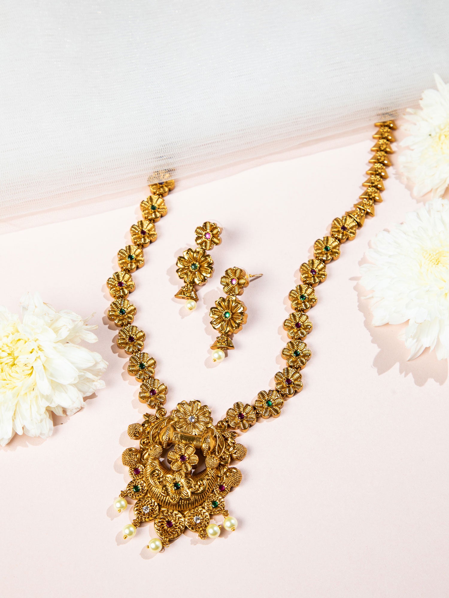 Gold temple necklace set and earrings set on a light pink background with flowers