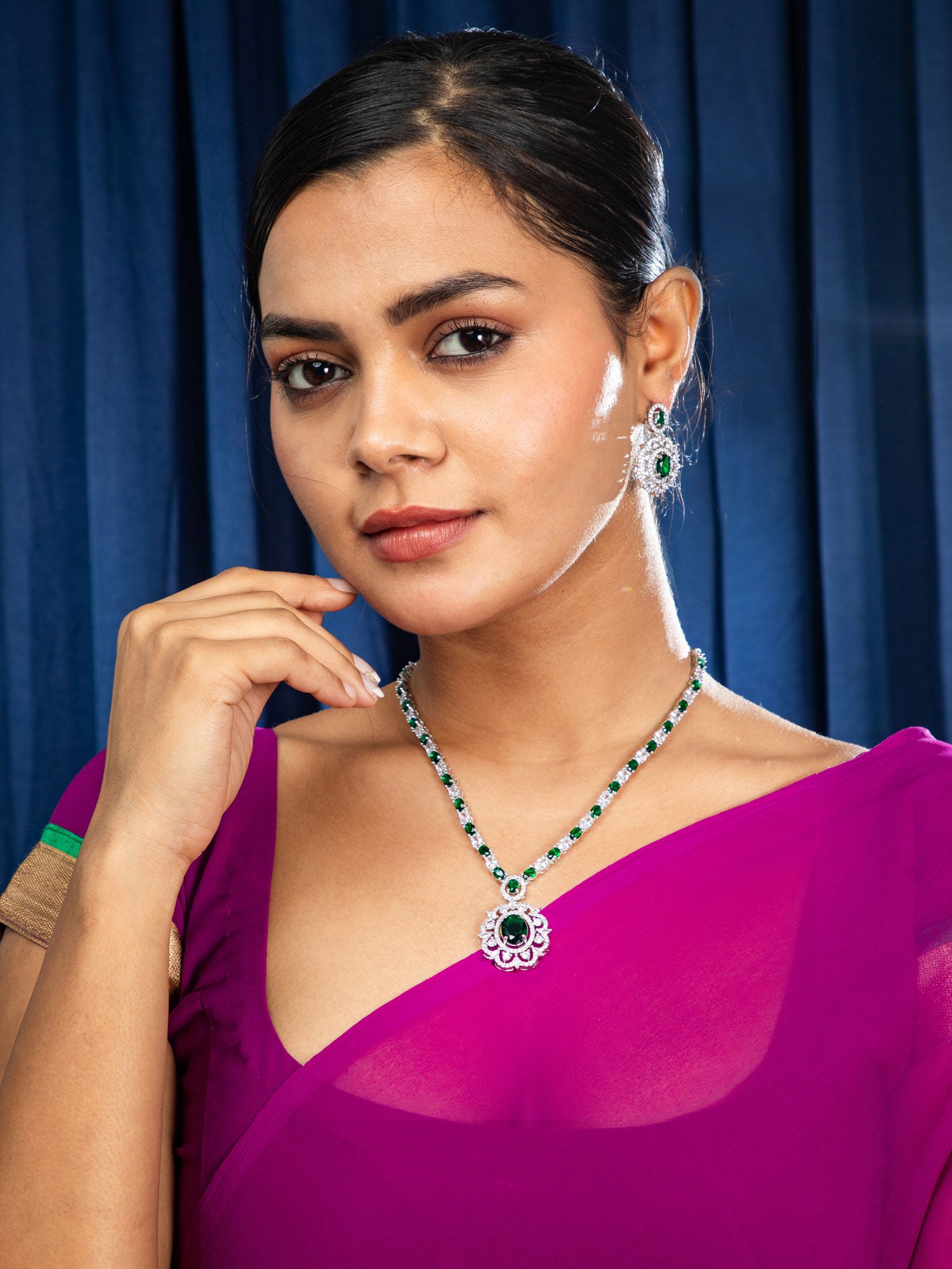 Woman wearing a purple saree with jewelry against a blue curtain background