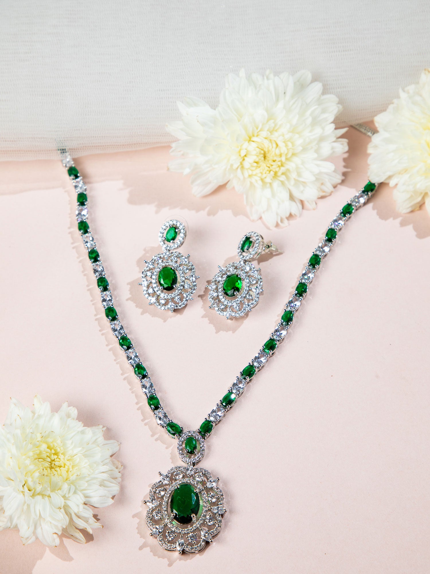 pendant and earring with emerald green stones on a pink surface with white flowers.
