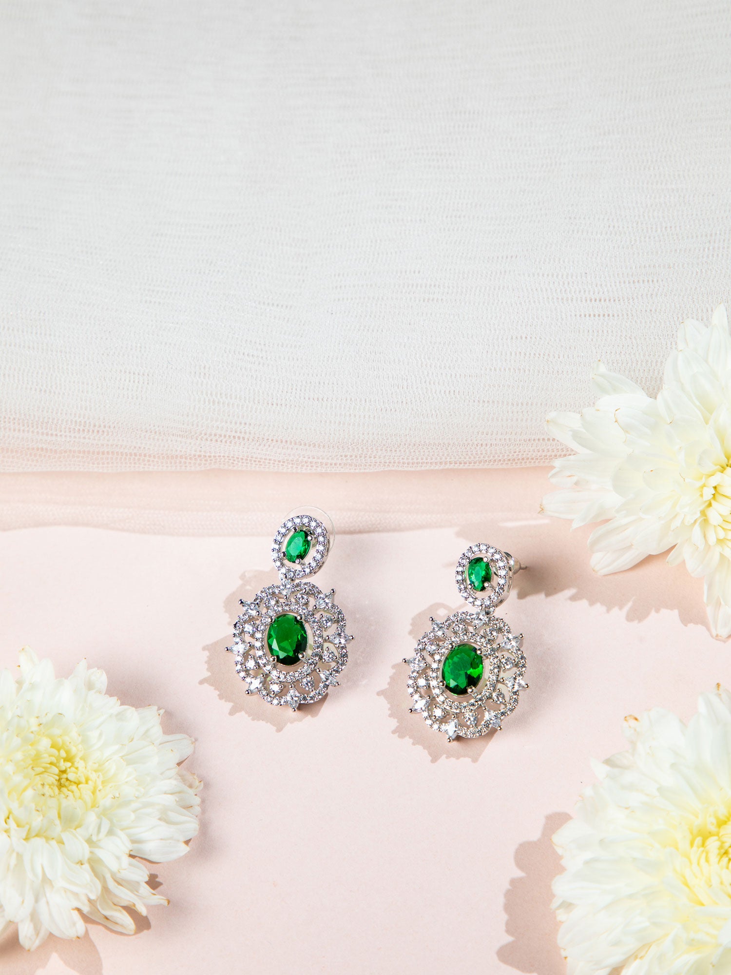 Pair of earrings with green gemstones on a pink surface with flowers