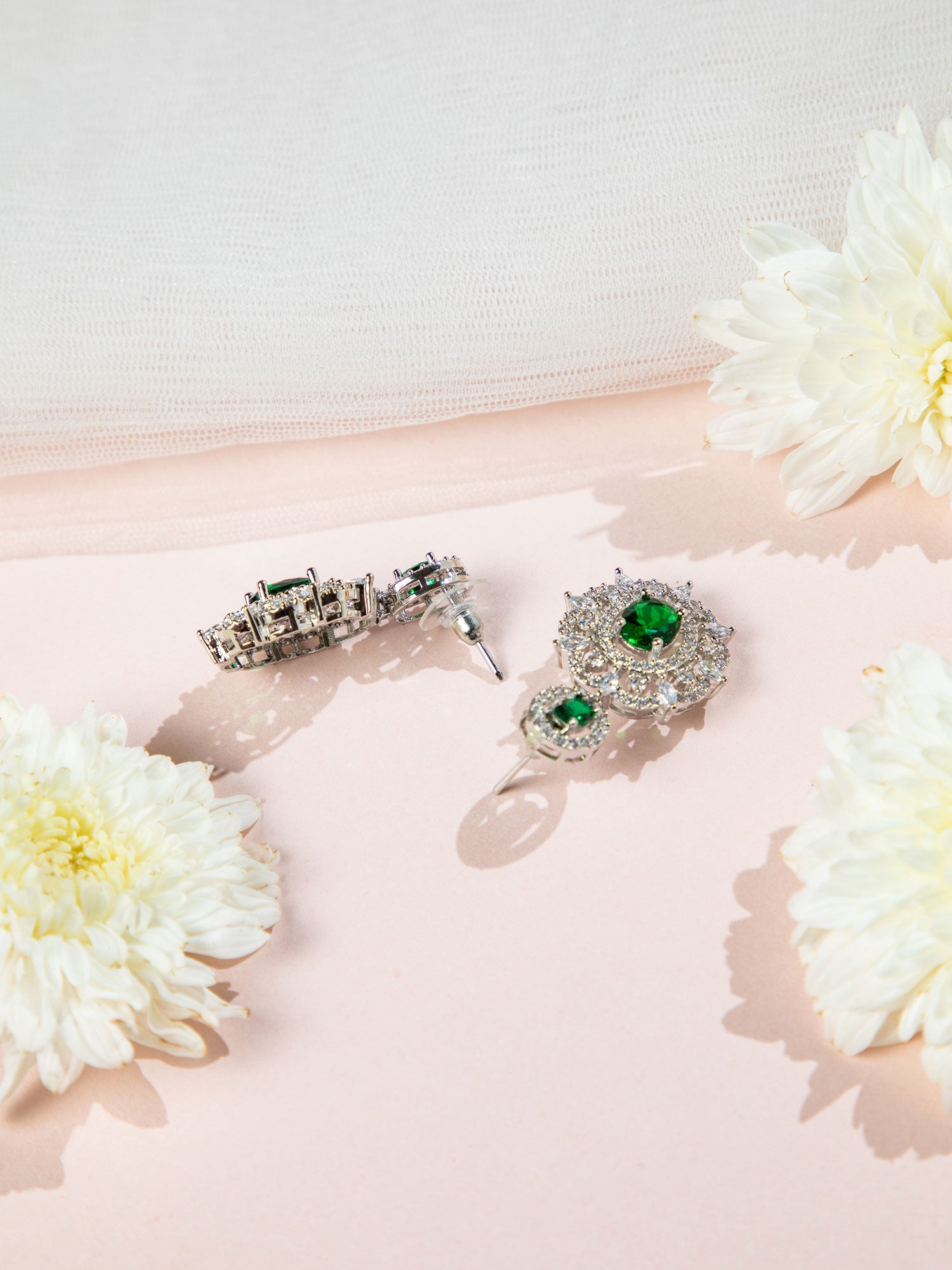 Pair of silver earrings with green gemstones on a pink surface with white flowers.