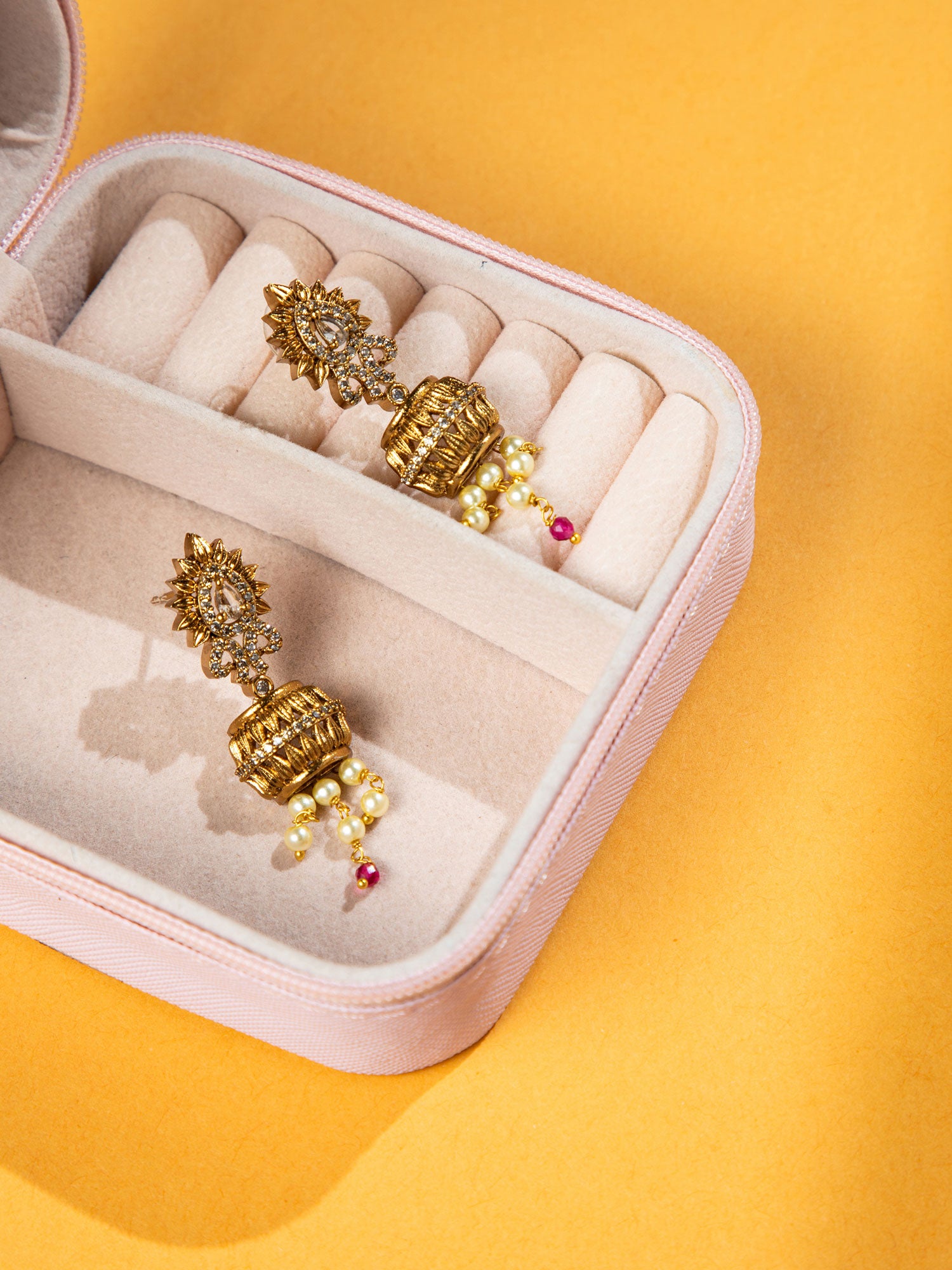 Gold earrings in a pink jewelry box on a yellow background