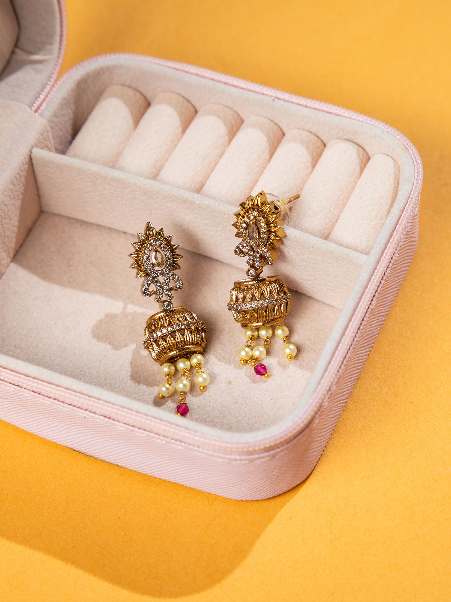 Gold earrings with pearl-like beads in a jewelry box on a yellow background