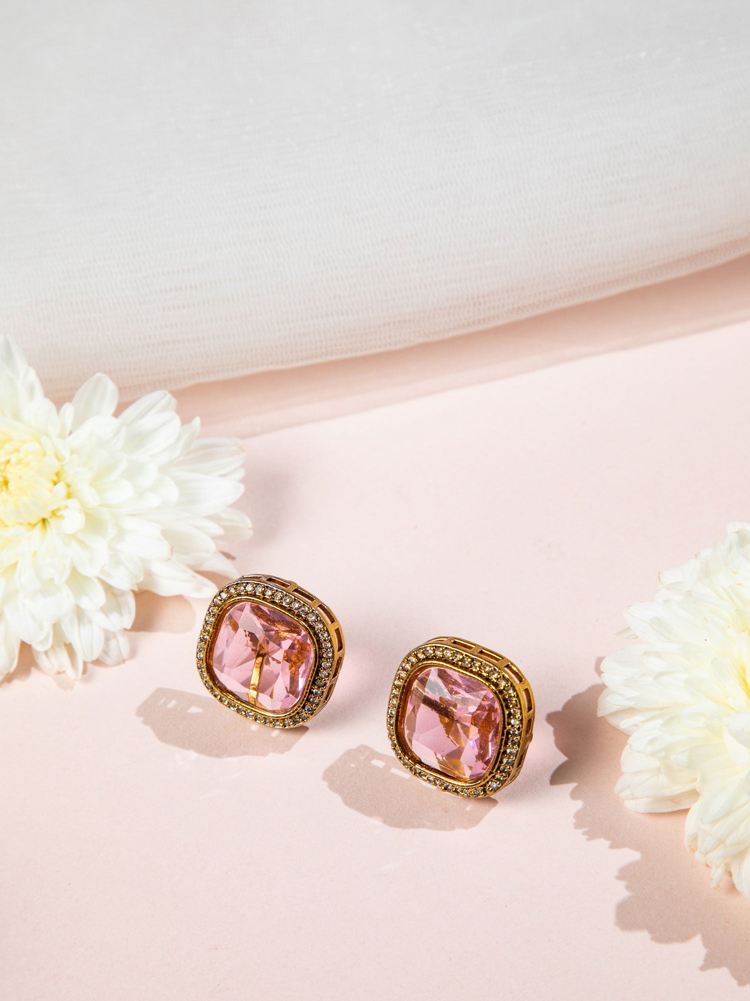 Pink earrings with gold accents on a pink surface with white flowers