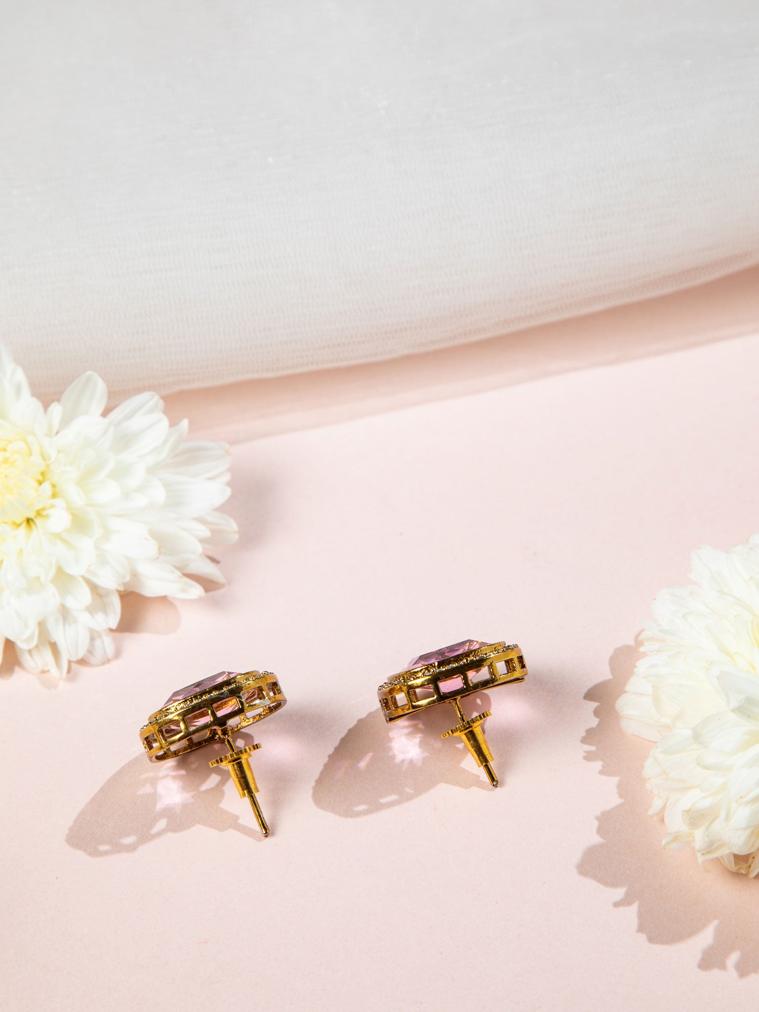 Pair of gold and pink earrings on a light pink surface with white flowers.
