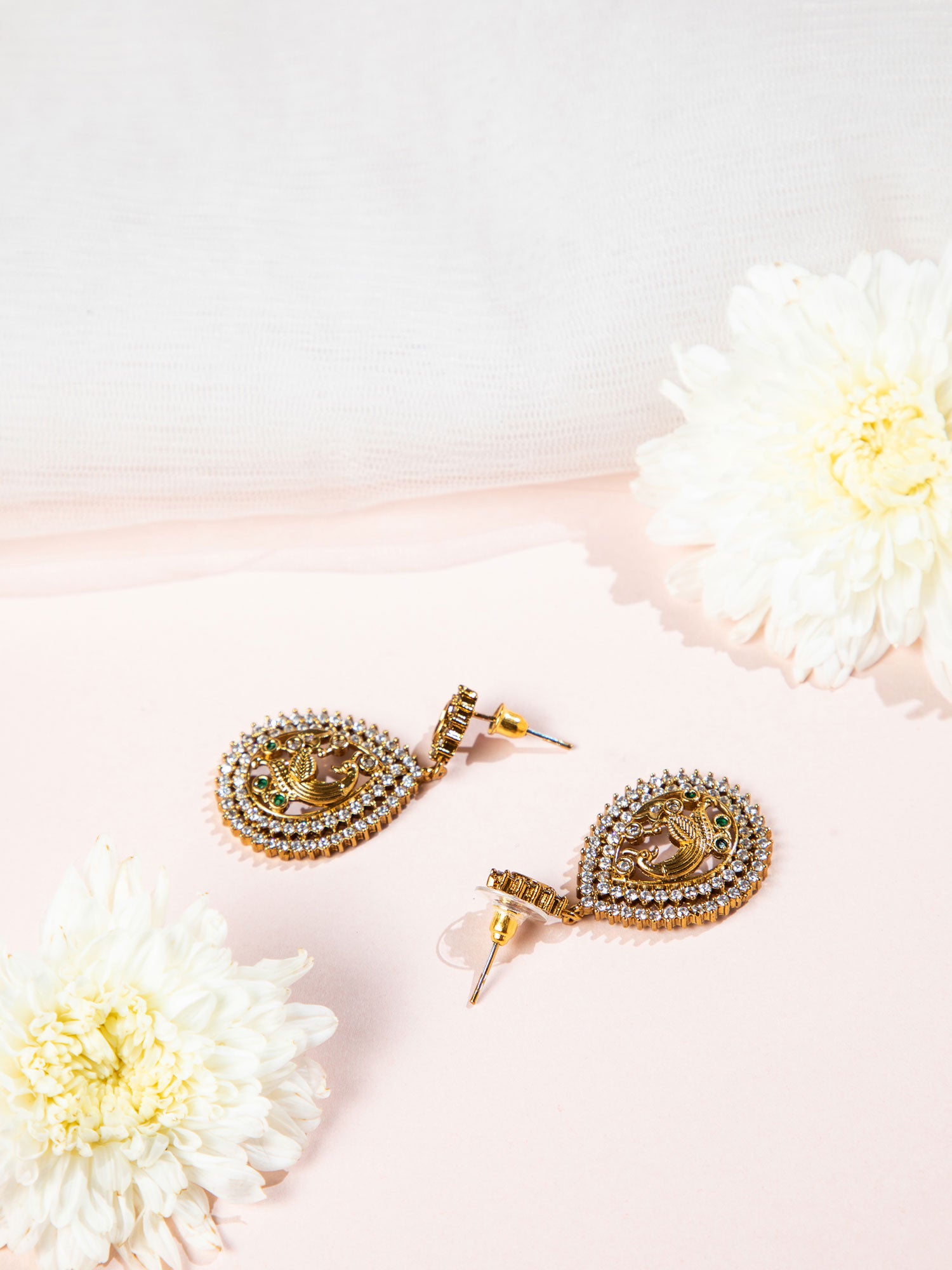 Gold earrings with intricate designs on a light pink background with flowers.