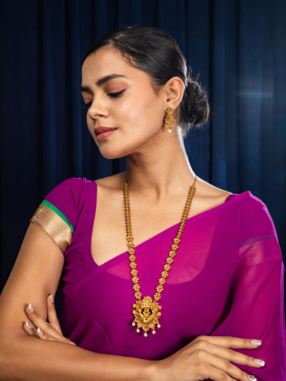 Woman wearing a purple saree with temple necklace set against a dark blue curtain