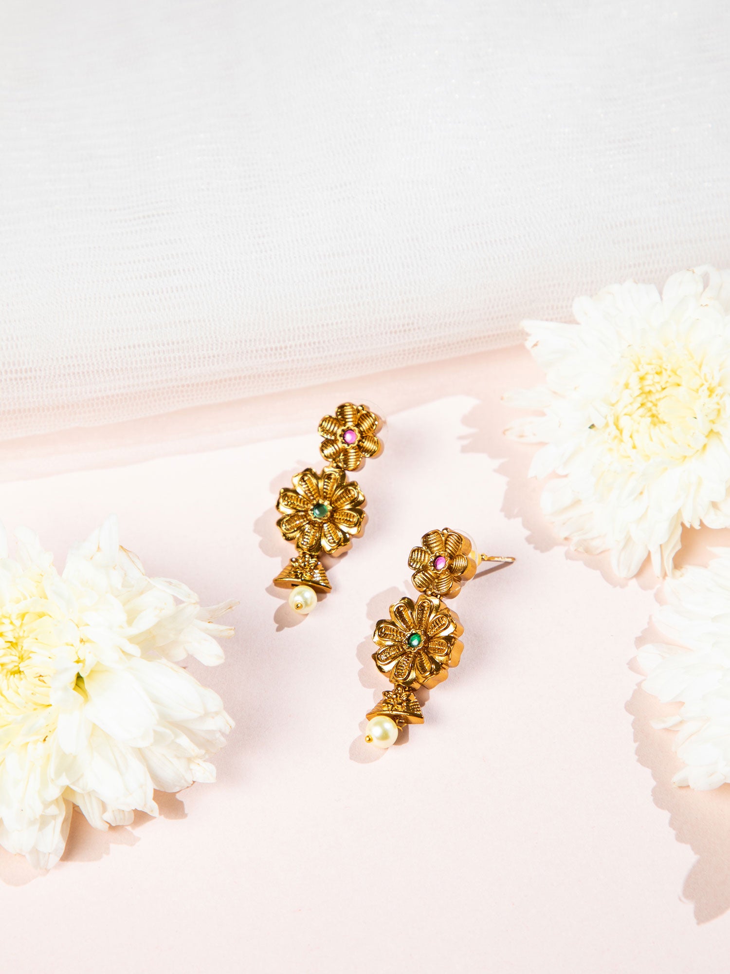 Gold floral earrings with white pearl centers on a light pink background with white flowers.