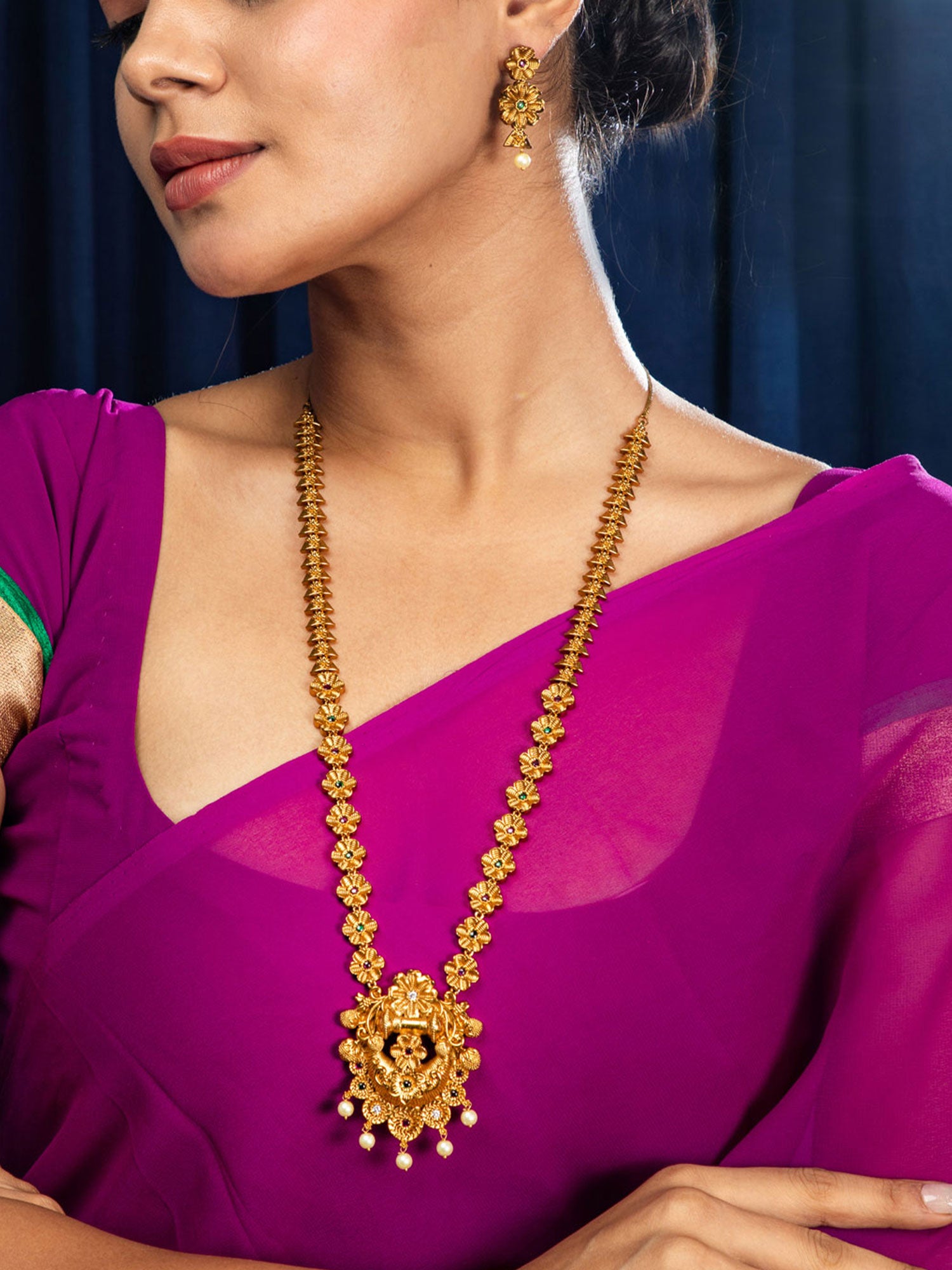 Woman wearing a gold necklace and earrings against a dark blue background