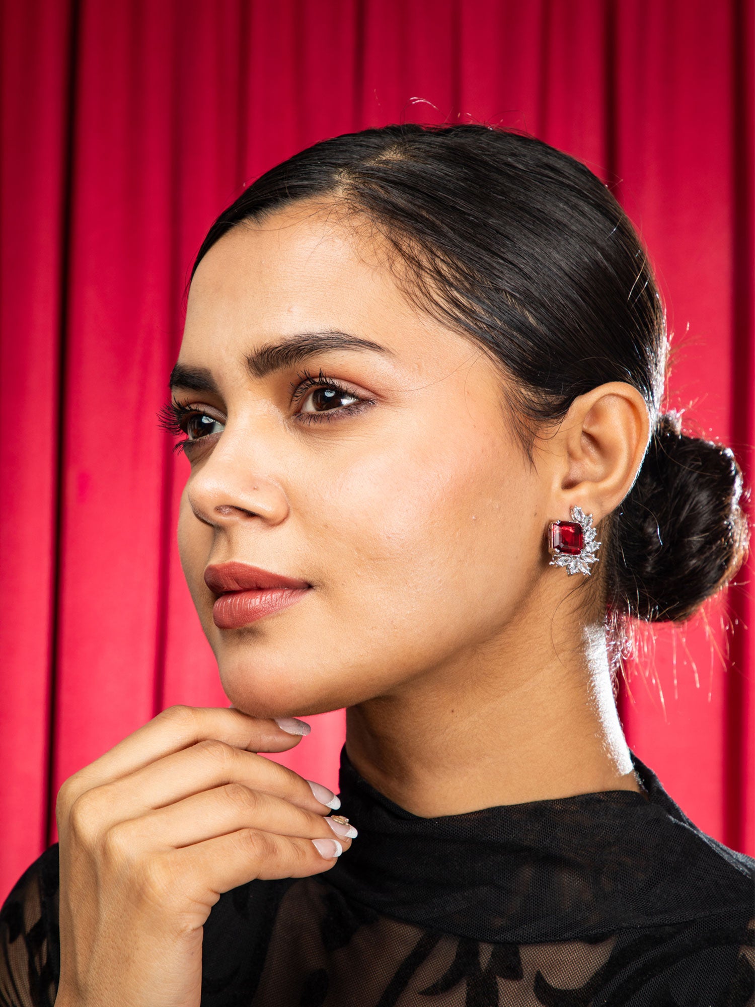 Woman wearing red stud earrings against a red curtain background