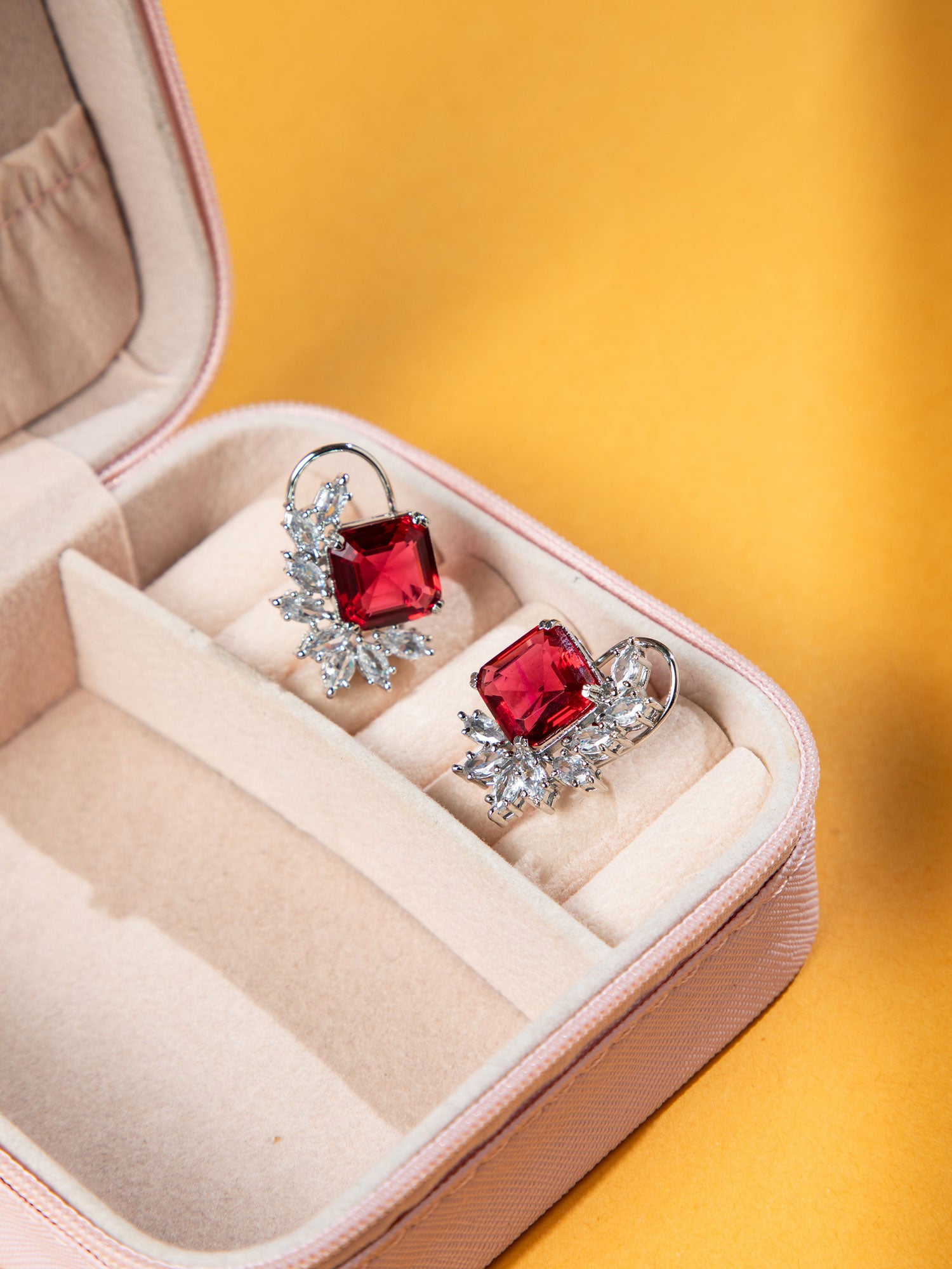 Pair of earrings with red Rhodium Studs in a jewelry box on a yellow background