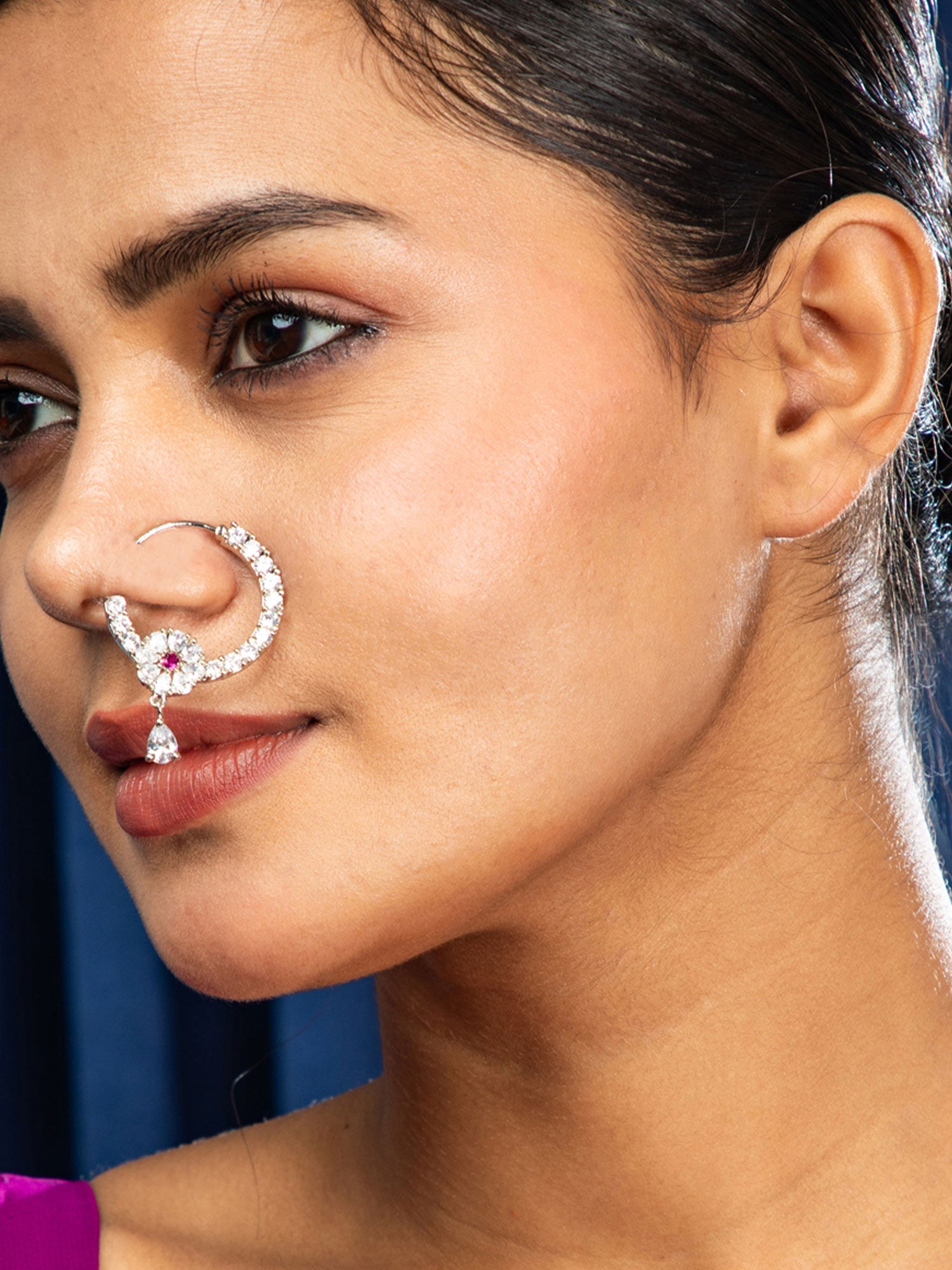 Close-up of a woman wearing a nose ring with a purple background